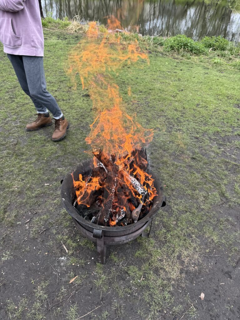 Small fire pit, half of Emmett in background, large orange flame. 