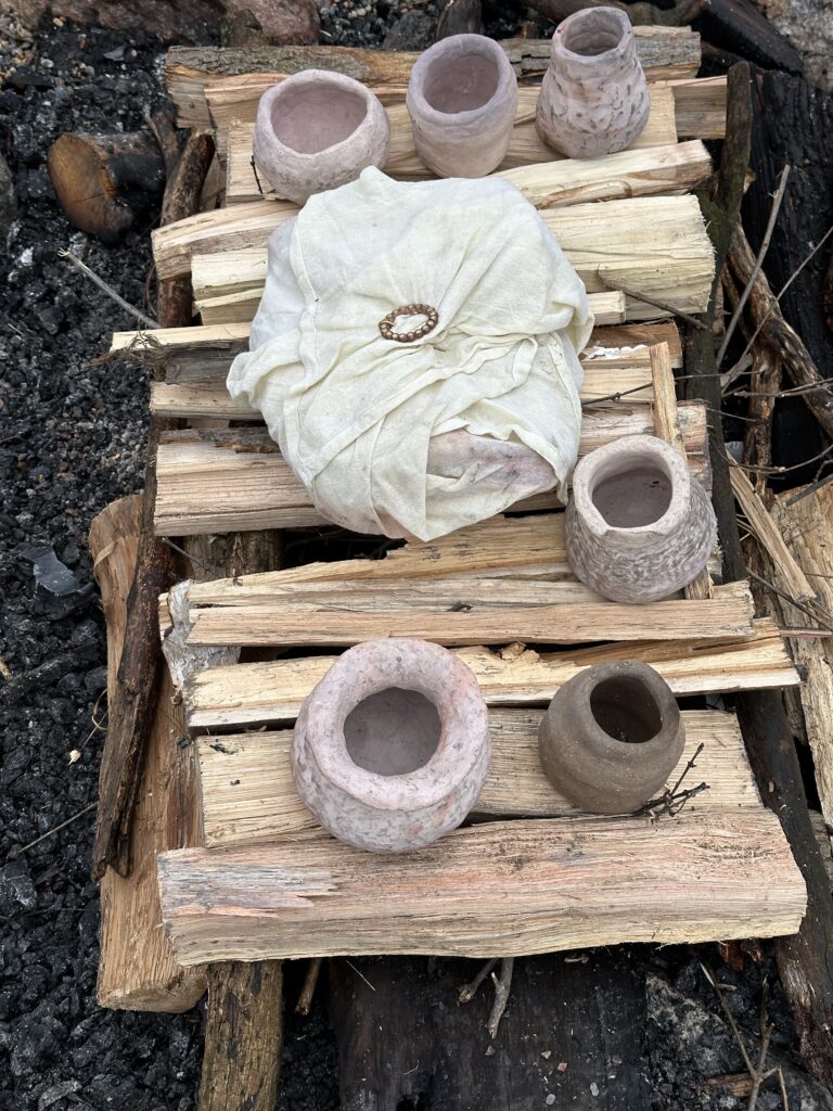 Bundle of the lamb shoulder surrounded by pre-fired clay pots on horizontal platform in funeral pyre.