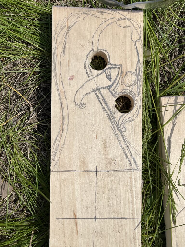 Piece of wood with pencil marks showing a dragon, 2 holes punched within the animal for eyes, and measurement marks at the bottom of the image
