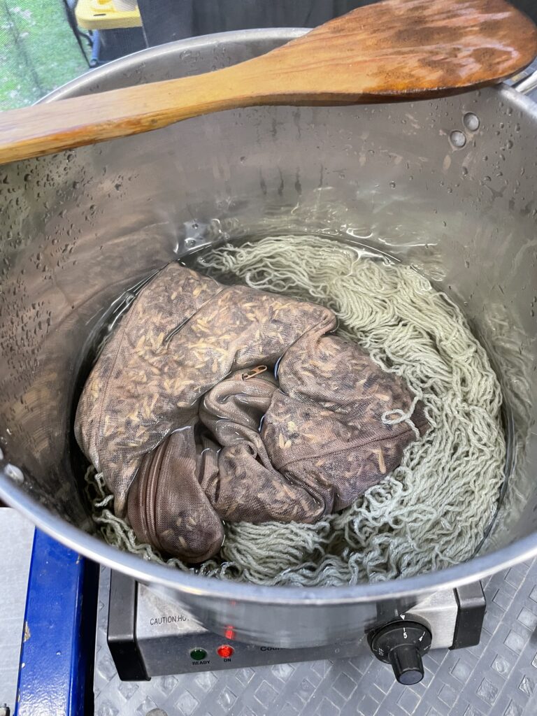 Yarn during the dying process: pale green yarn and bag of woad seeds in metal pot.